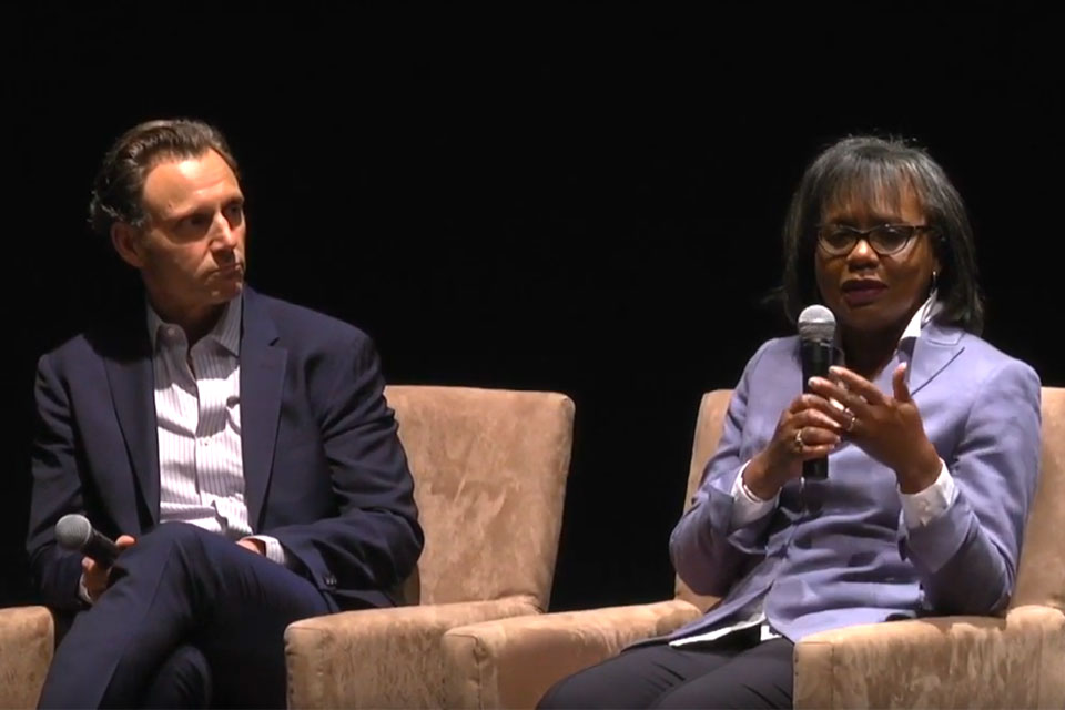 Tony Goldwyn and Anita Hill sit on stage holding microphones