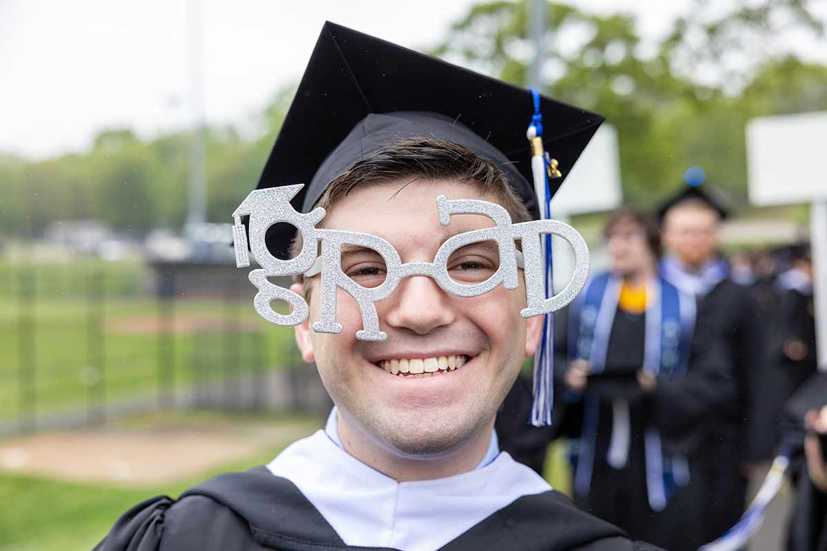 A person wearing silver sparkly glasses that read "Grad"