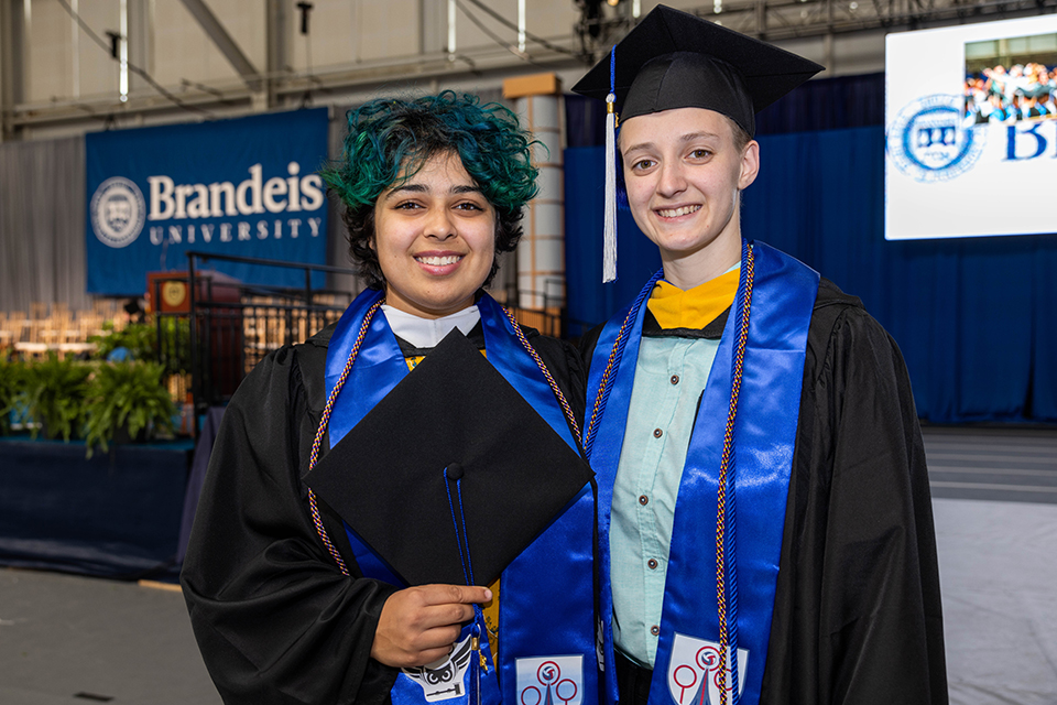 Two students pose and smile for the camera in graduation regalia.