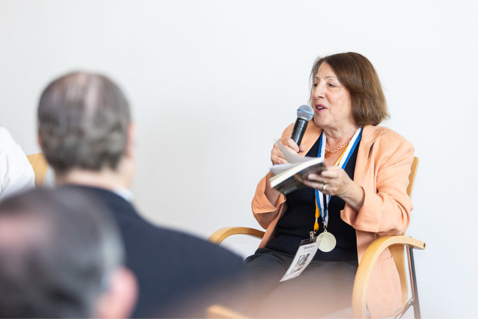 Woman in peach blazer seating with microphone in front of the crowd