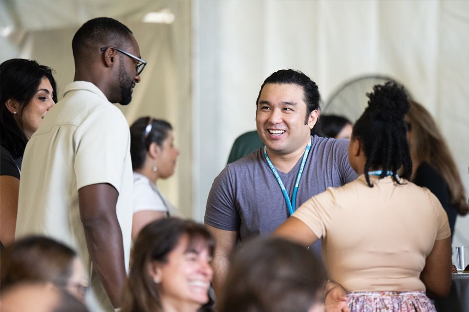 Group of three alumni chatting and smiling in the tent
