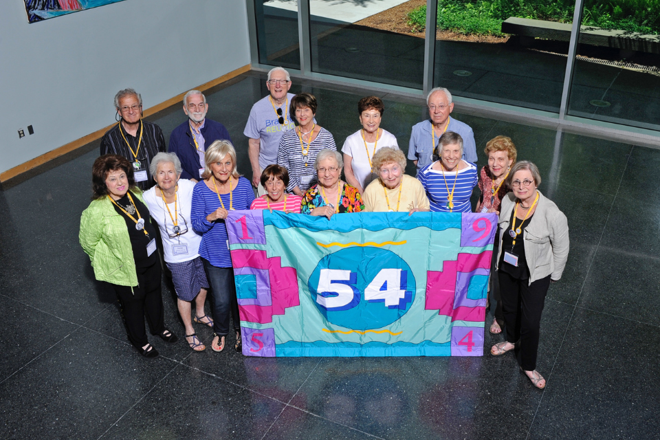 group of alumni from class of 1954 holding colorful flag