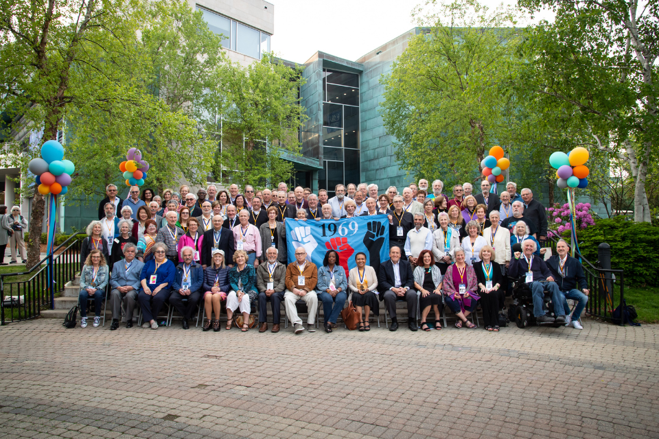 group of brandeis class of 1969 alumni gathered holding holding colorful class flag