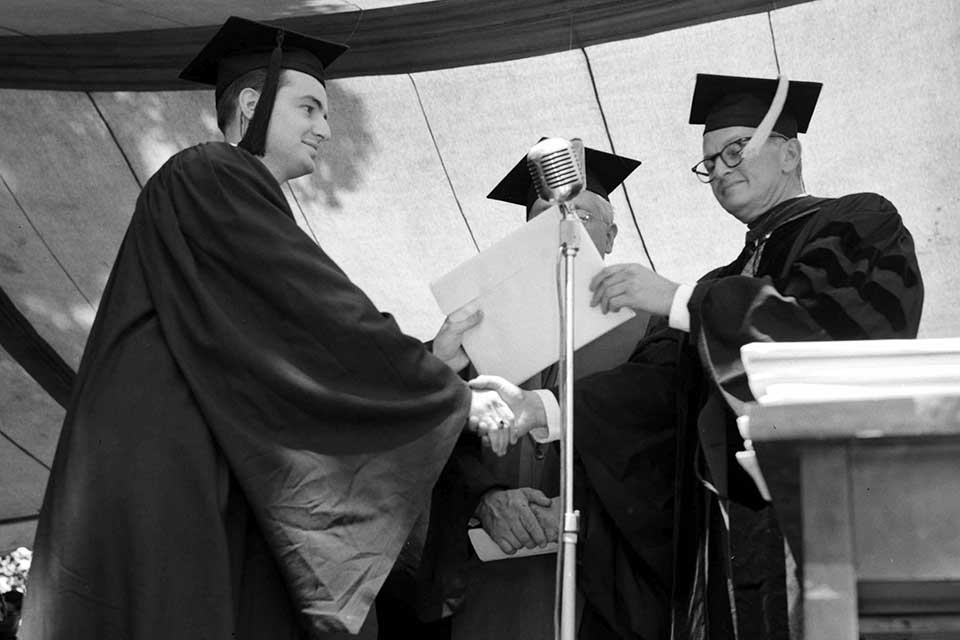 Male graduate shakes hands as he receives his degree.