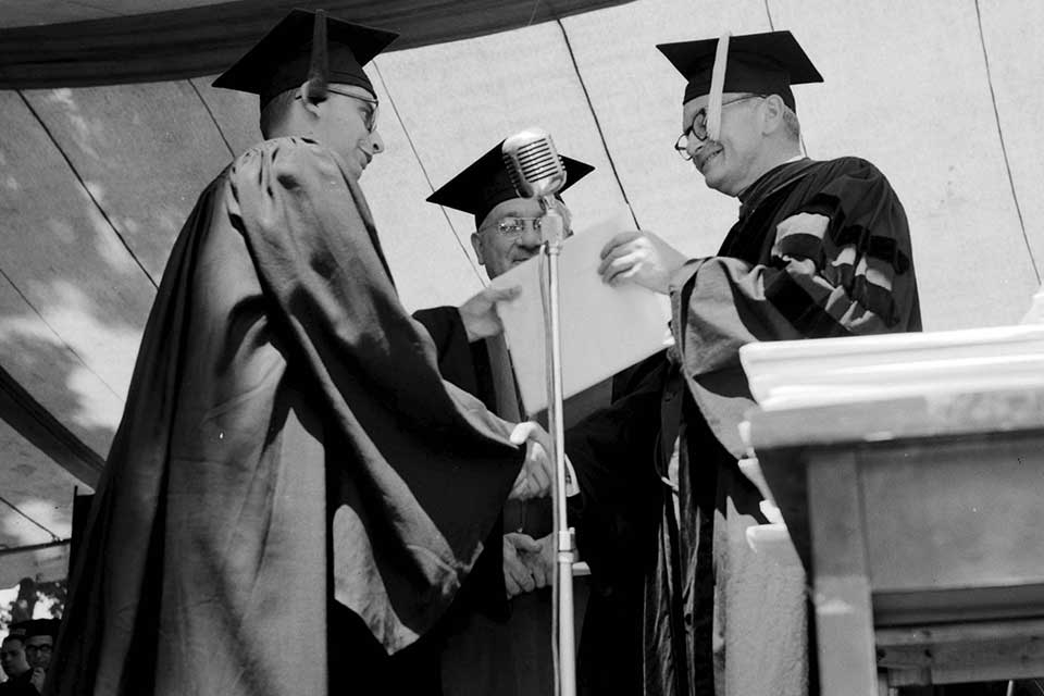 Male graduate shakes hands while receiving diploma