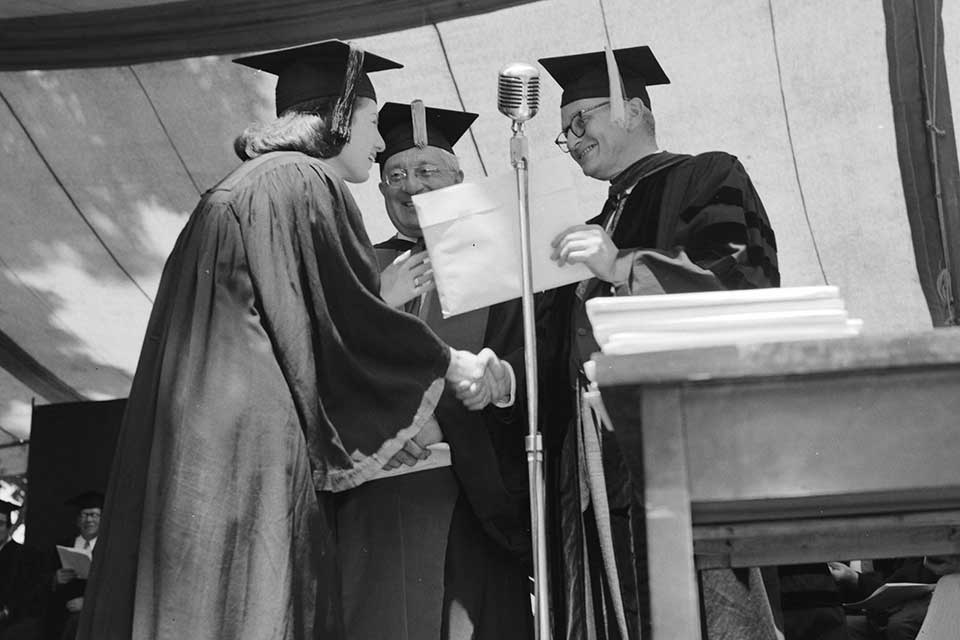 Female graduate shakes hands while receiving her diploma.
