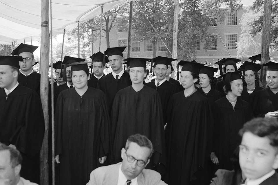Group of male and female graduates stand in a crowd.