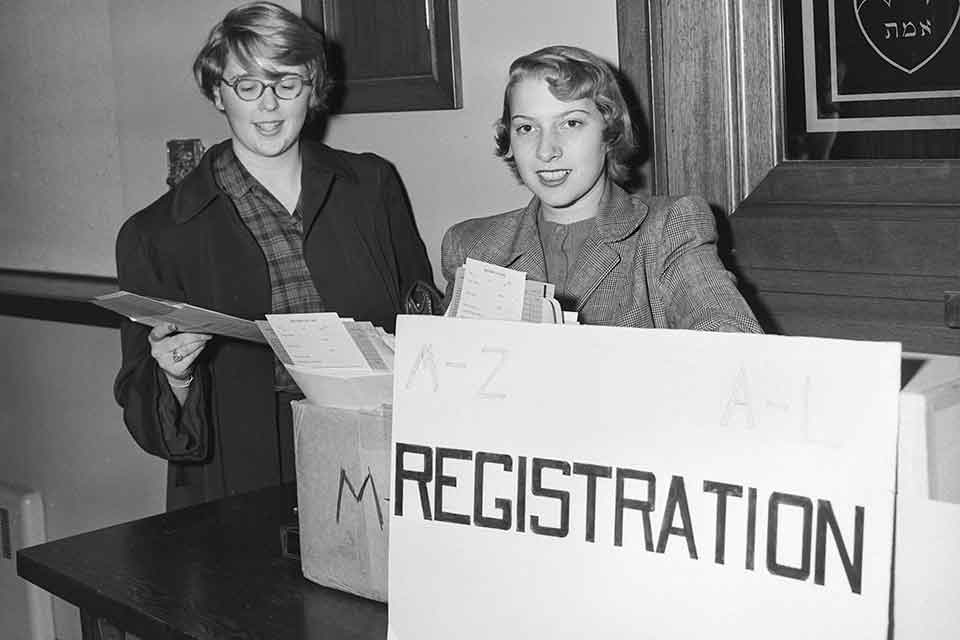 Two female students standing behind a sign that says "Registration"