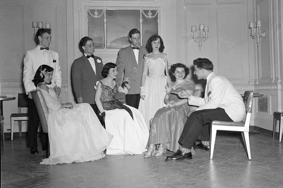 Students sitting and standing in a group, in formal dress, chatting and laughing.