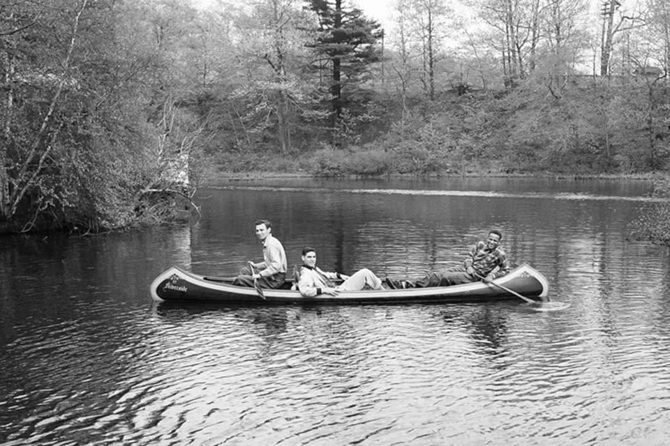 Three male students lounging in a canoe on a pond. 
