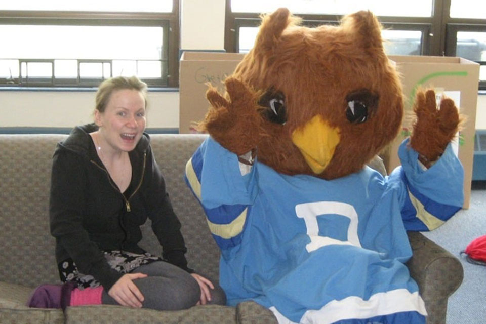 Woman sitting on a couch and smiling with an Owl mascot.