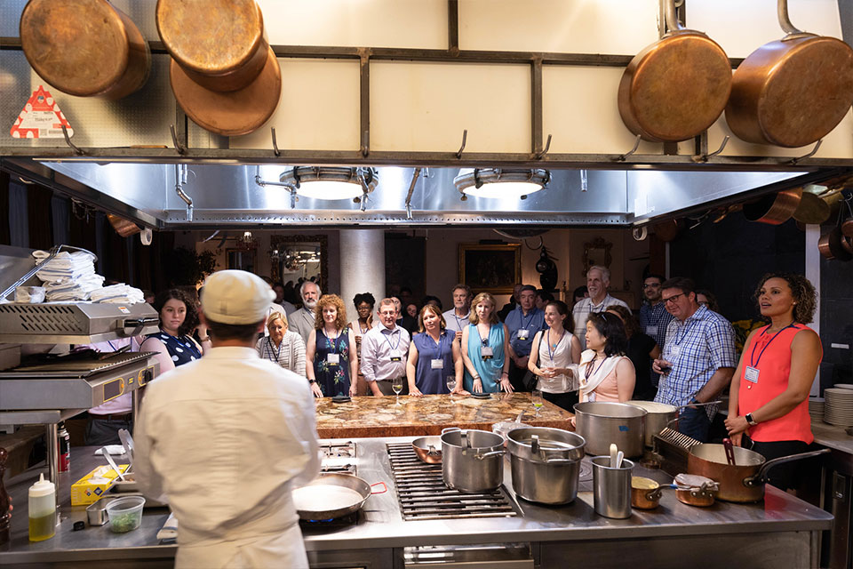 A chef speaks to a group of Brandeis alumni in an industrial kitchen