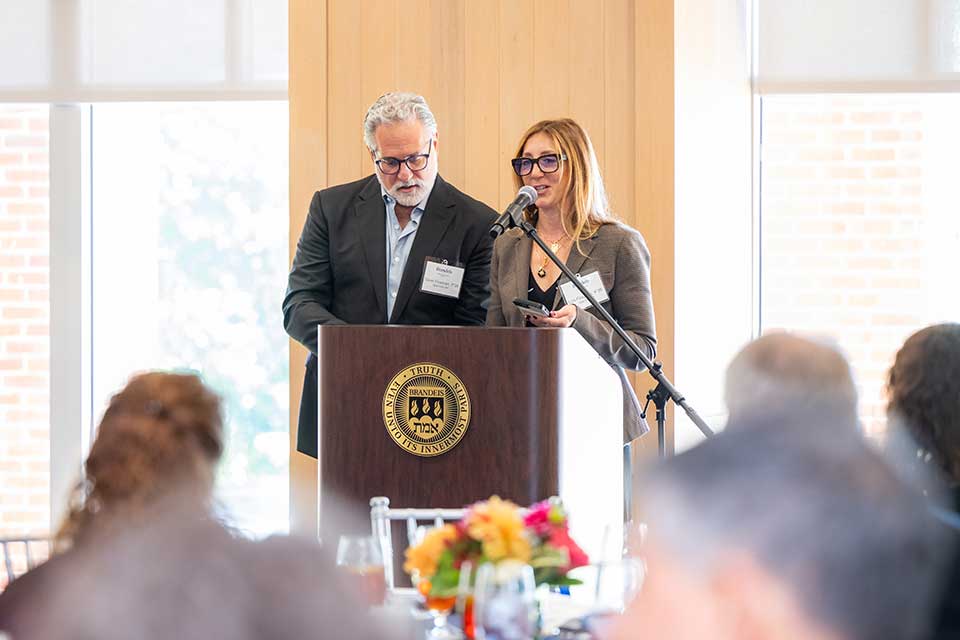 Two people stand at a podium and address an audience.