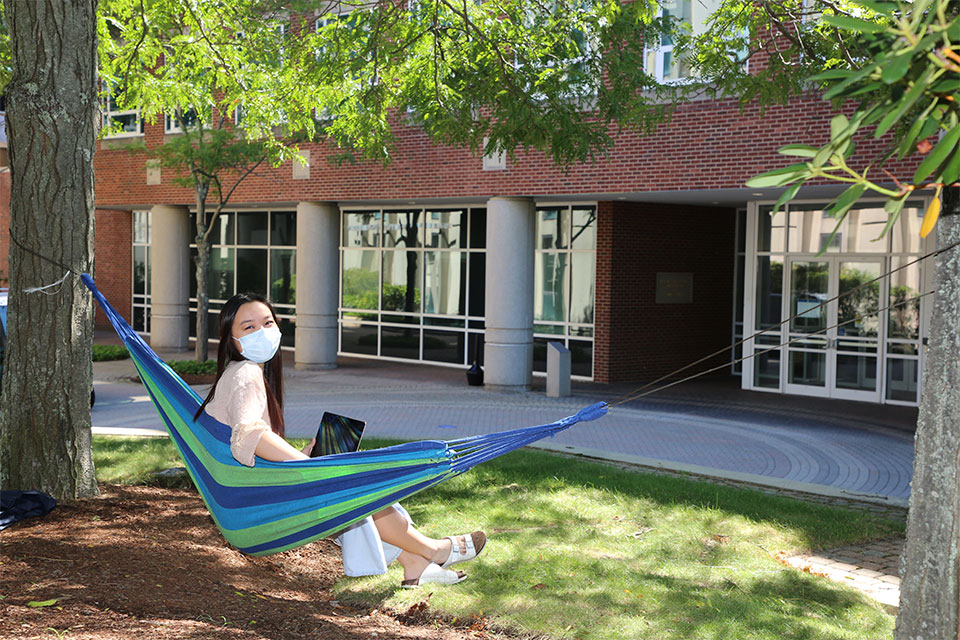 student wearing mask sits on hammock with laptop