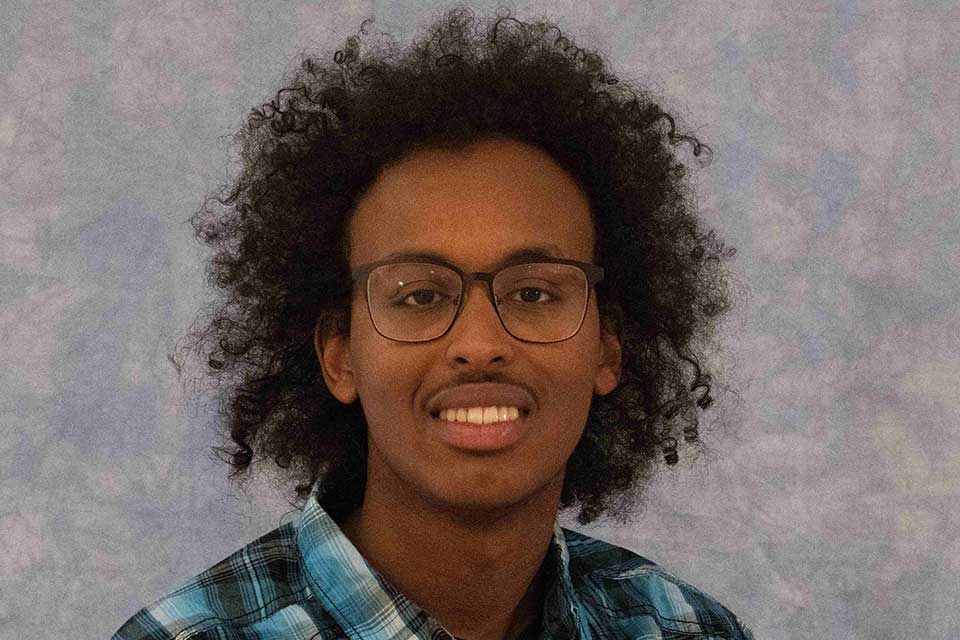 Young Black man with glasses smiles at the camera. 