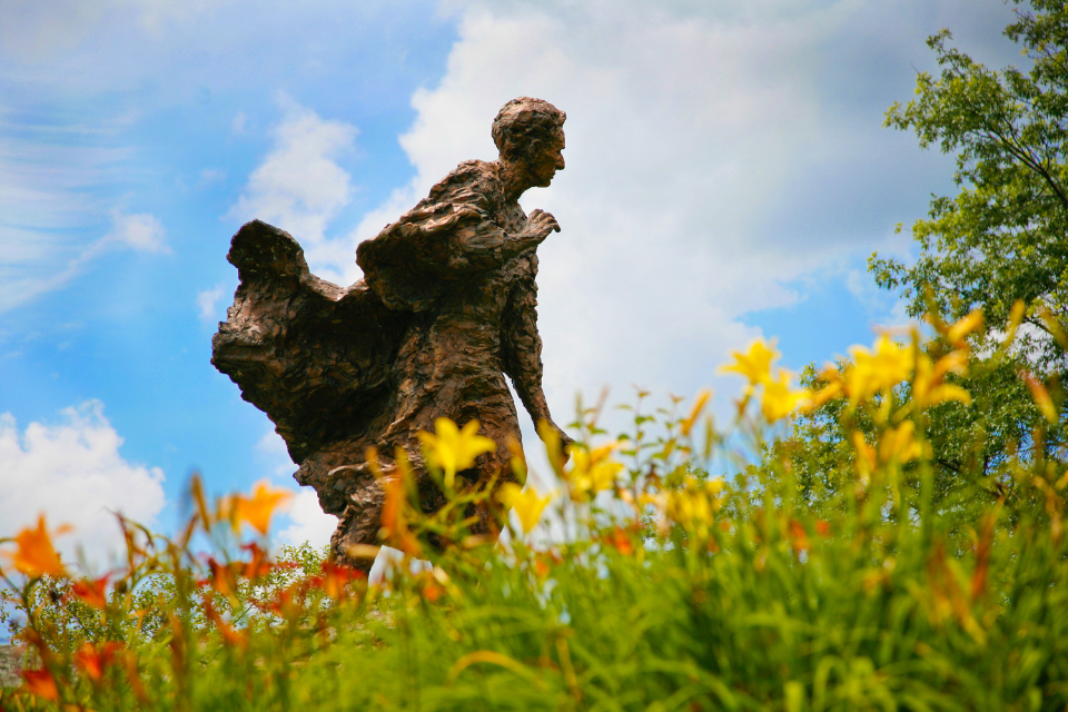 Louis Brandeis statue against a blue sky with white clouds. Yellow and orange lillies cover the foreground of the photo.