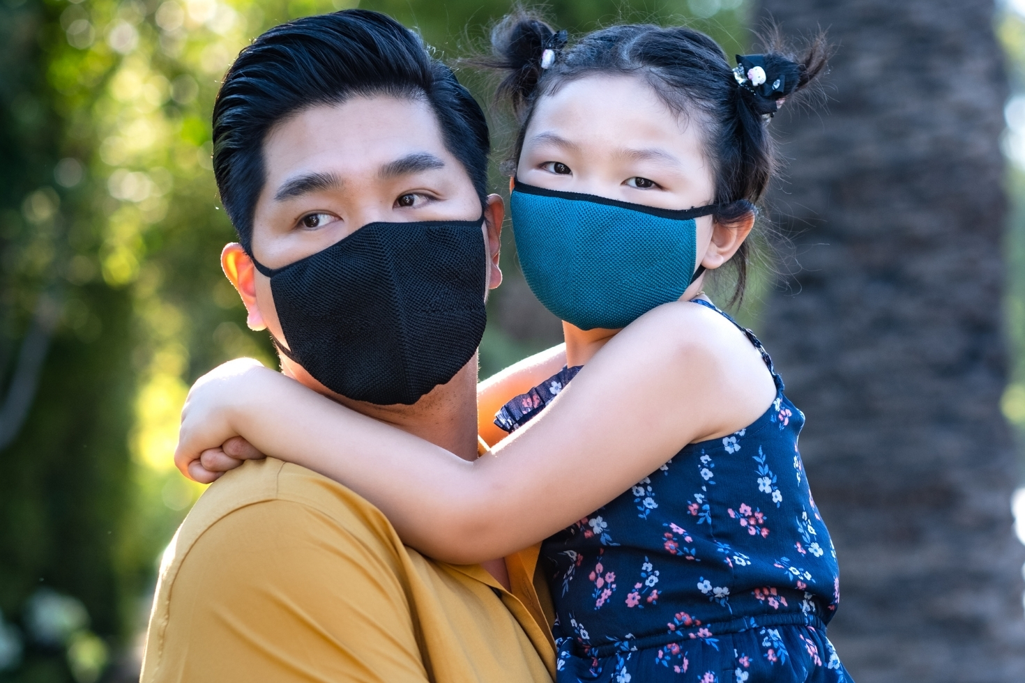 Father holding daughter, both wearing masks