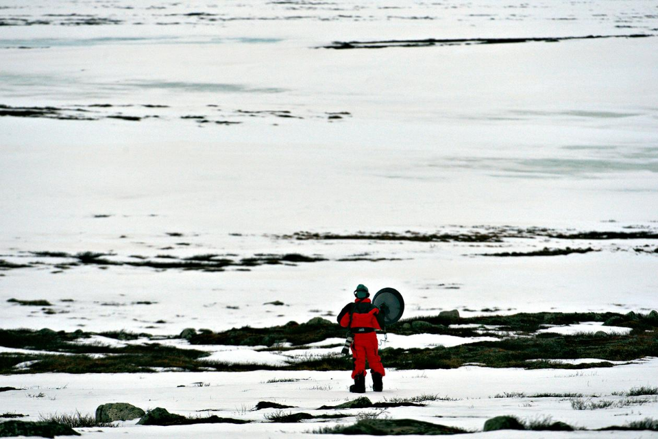 person in red snow gear holding professional camera amidst vast snowy terrain