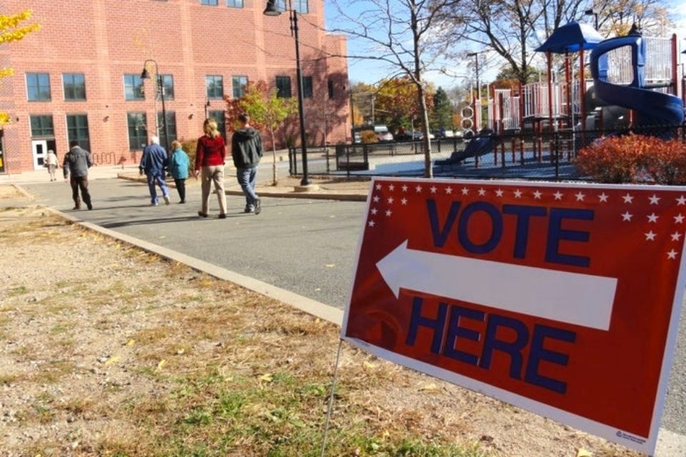 A sign that says "Vote here" next to people walking into a polling place