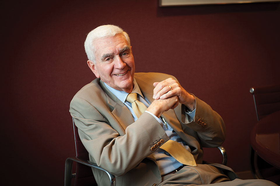 Earle Kazis, seated, in a suit, smiling