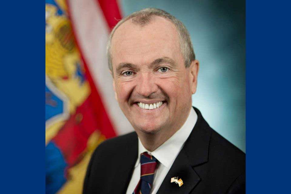 Governor Phil Murphy of New Jersey seated in front of the state flag