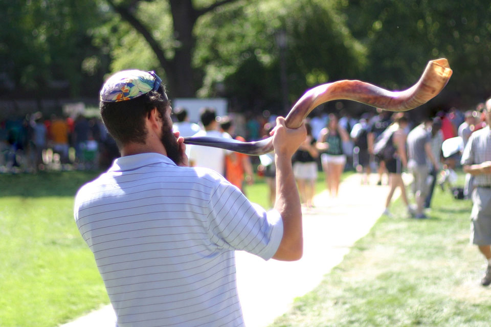 From back: Man wearing a yamulka blowing a shofar