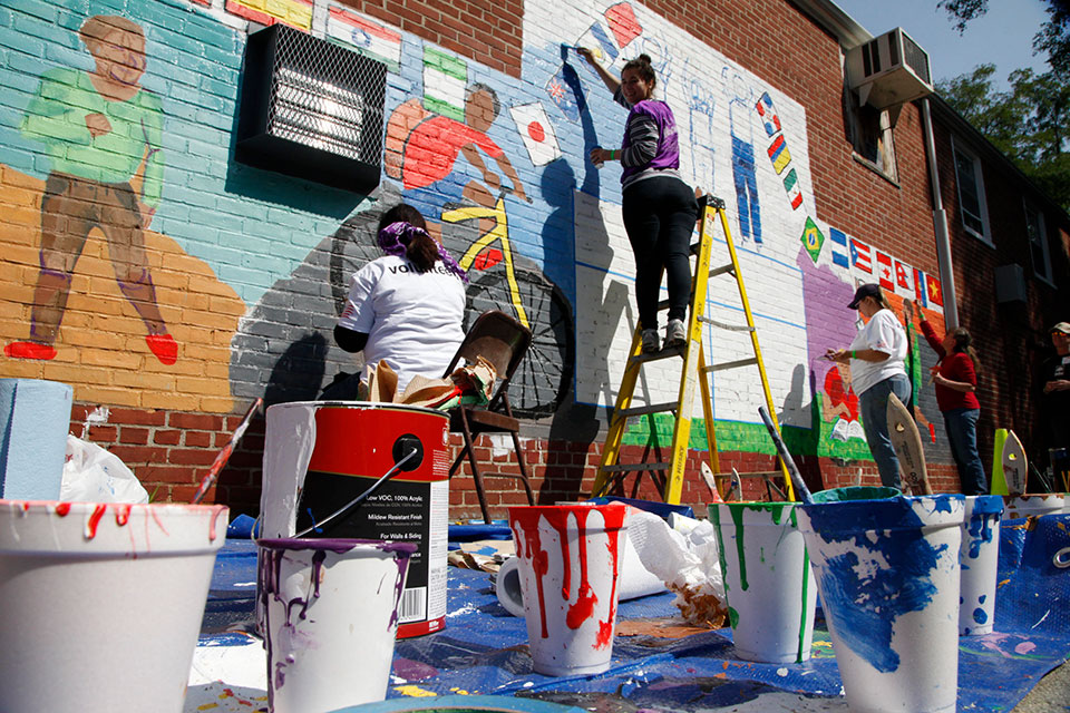 Members of the Waltham Group paint a colorful mural on the side of a building.