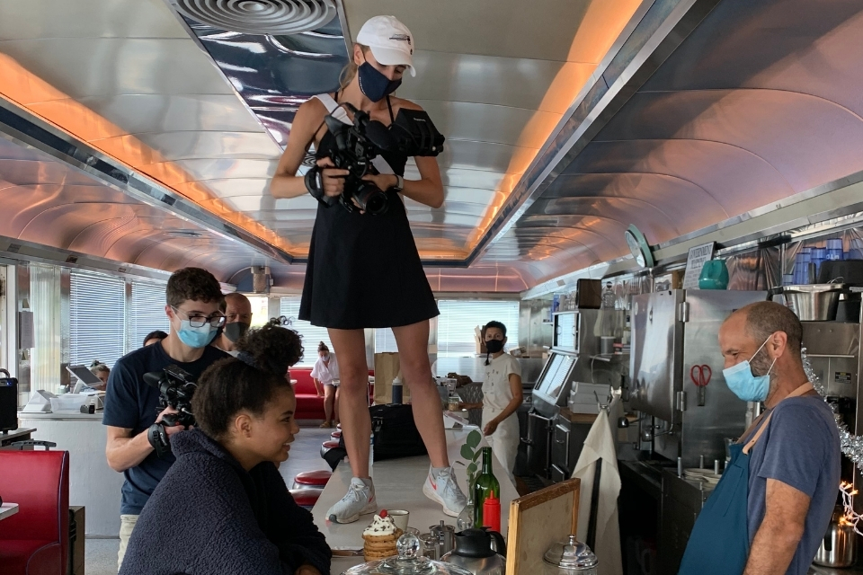 Elizabeth Cayouette holding a camera, standing on the counter of a restaurant.