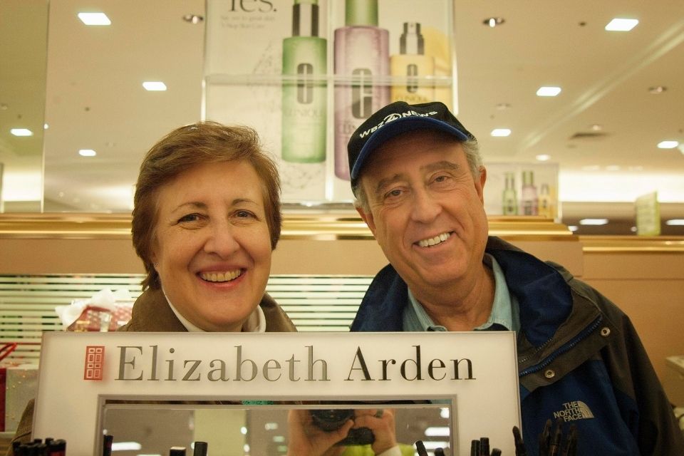 Ann Carol Grossman and Arnie Reisman smiling behind an Elizabeth Arden sign in department store