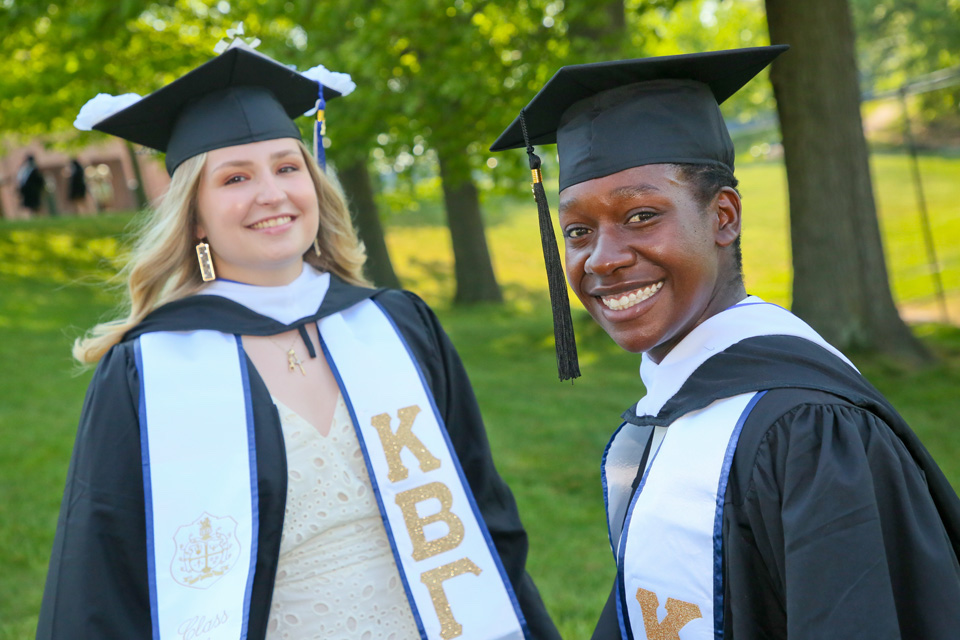 Two students in caps and gowns and stoles smiling
