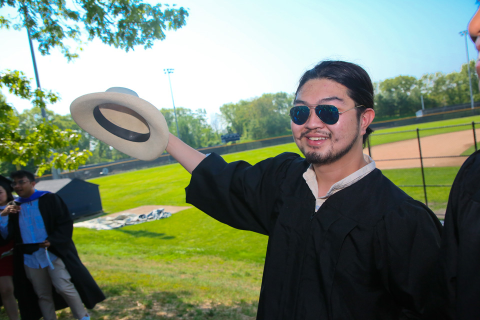 Student in a gown holds a straw hat out to his right