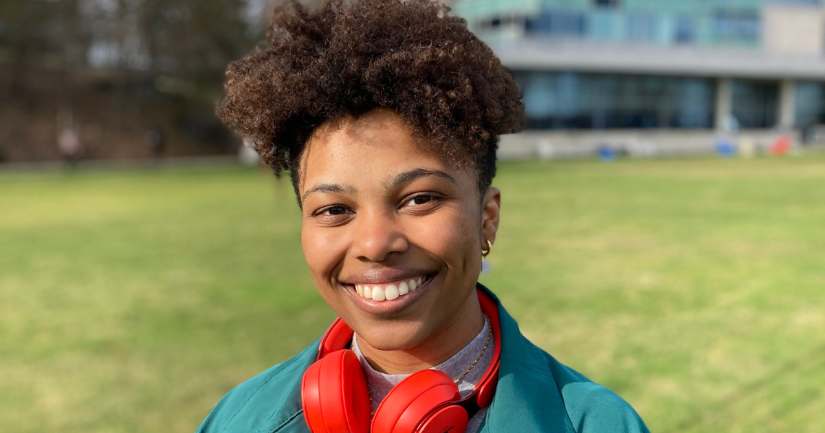 Black female student with red headphones around her neck smiles at the camera.