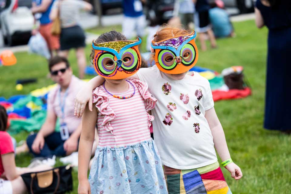 Two little girls with arms around each other wearing masks they decorated. 