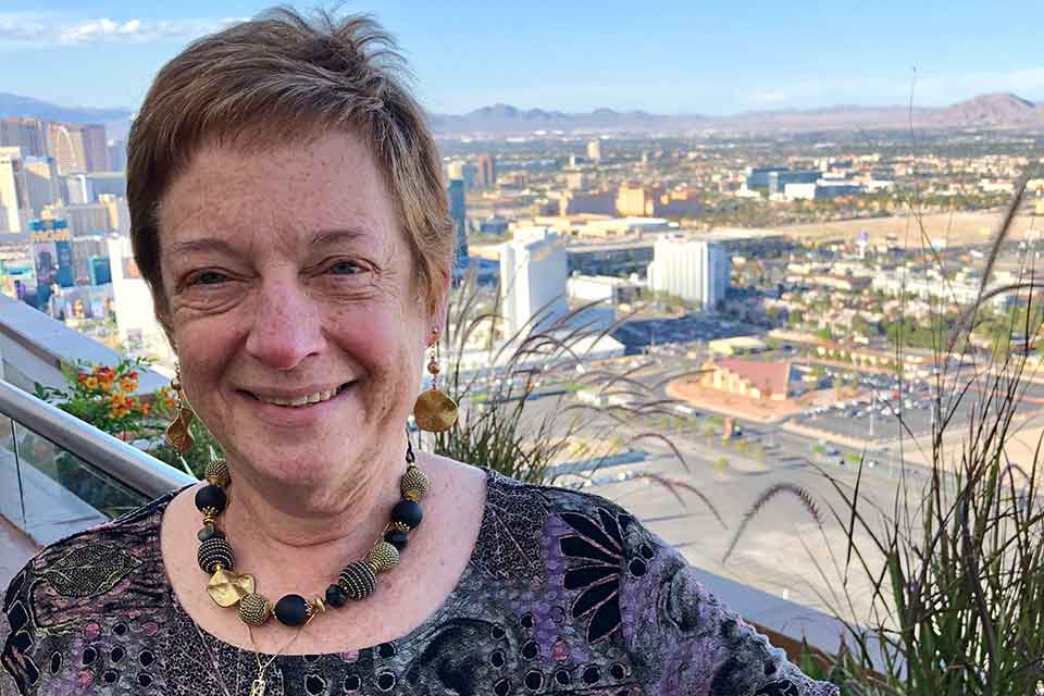 Susan Feigenbaum smiling and standing on a balcony with vista in the background