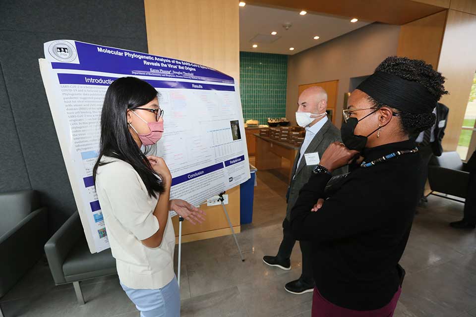 female student discussing her poster presentation with alumni scientists.