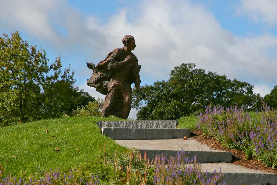 Statue of Louis Brandeis with flowering bushes and the text "Volunteer Leadership Convocation."