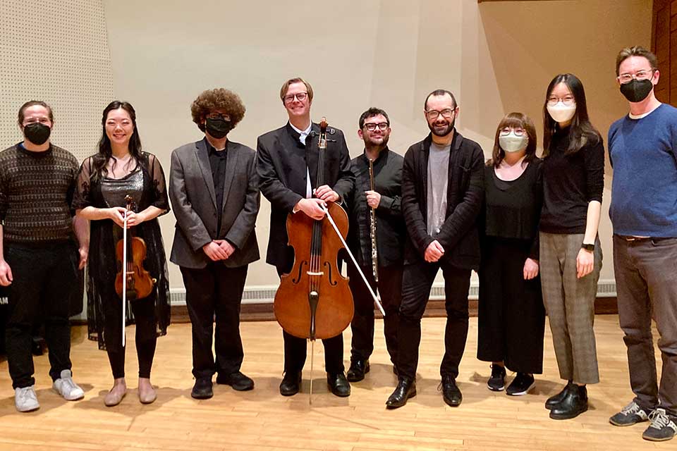 A group of Brandeis student composers standing with members of Hub New Music some holding instruments.