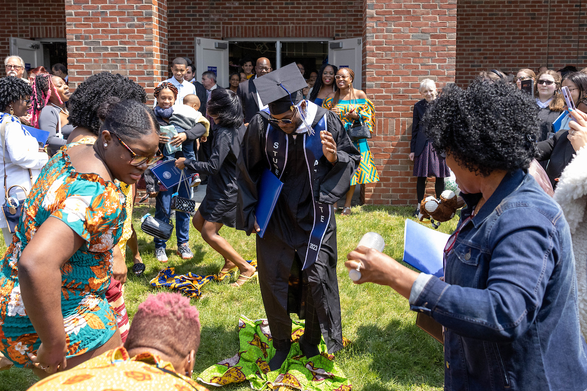 Terrell Brown dances as his family places fabric on the ground for him to walk upon, as part of a ceremony rooted in their Liberian culture celebrating accomplishments of loved ones, after the undergraduate Commencement ceremony.