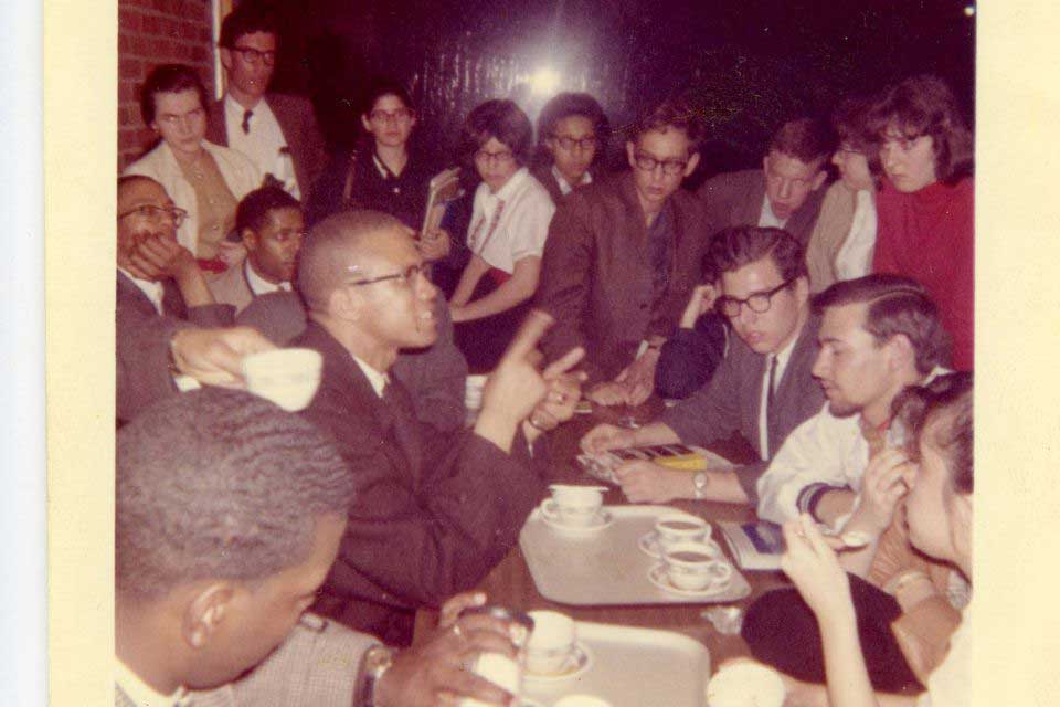 Malcolm X sitting at a table with students 