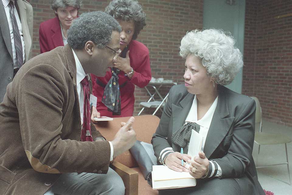 Toni Morrison signing a book while speaking to a man. 