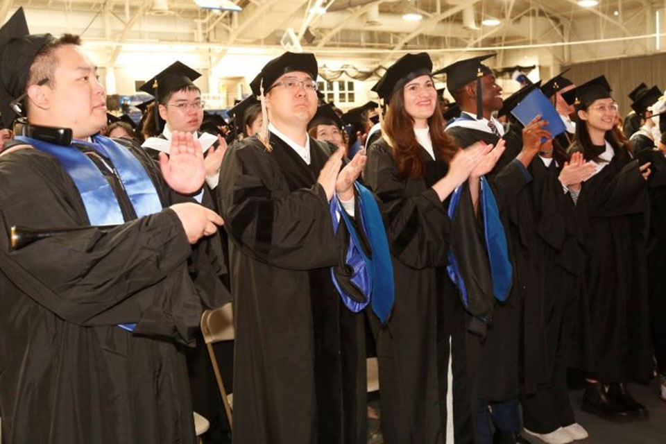 Graduates stand and clap during the Graduate Commencement ceremony