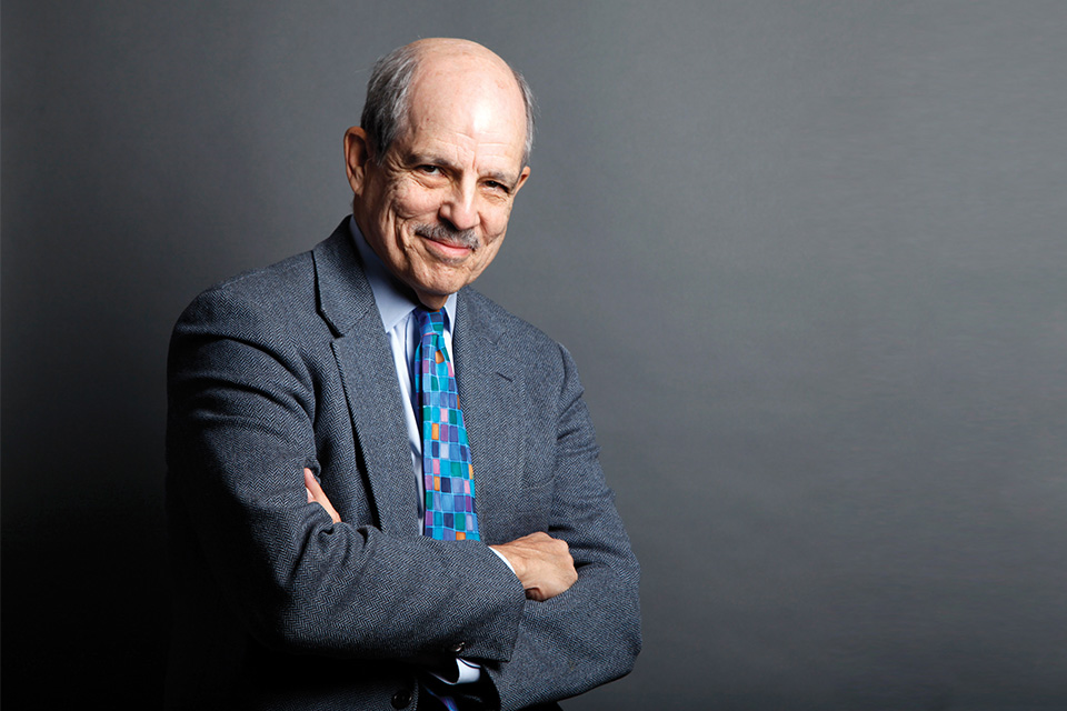 Paul Solman with his arms crossed on a grey background