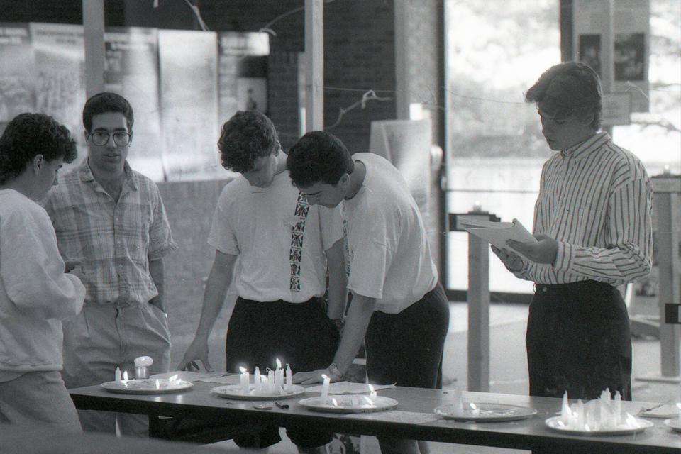 Black and white image of young male college students lighting candles at a table