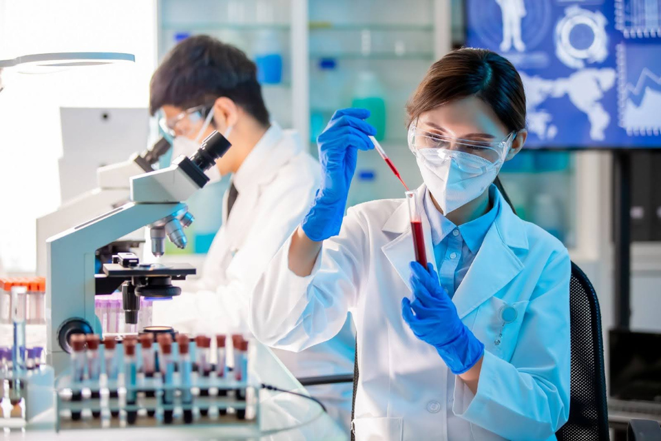 woman scientist in ppe holding a pipette of blod