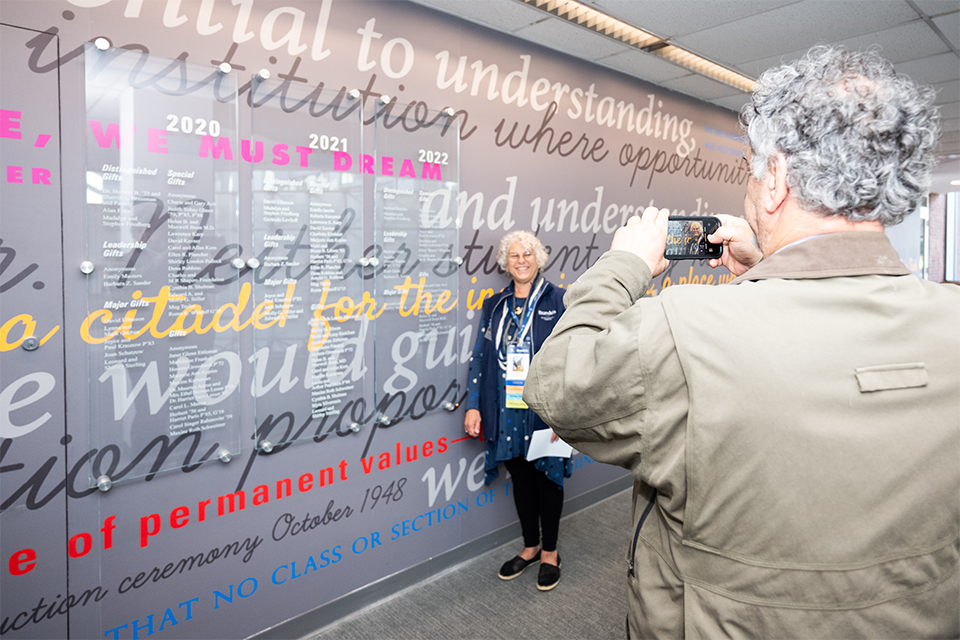 An alum taking a photo against the BNC Dedication Wall