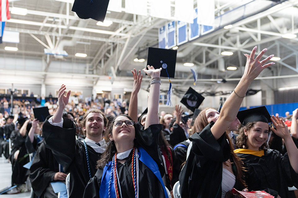 Graduating students dressed in academic regalia throw their caps in the air.