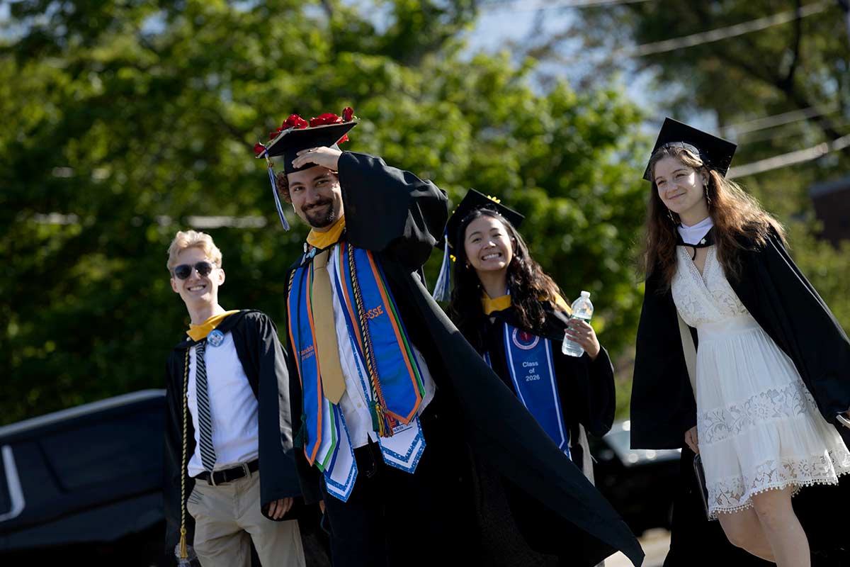 Graduating students dressed in academic regalia walk outside on campus.