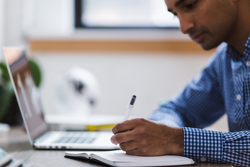 Person sits at a computer while writing something in a notebook