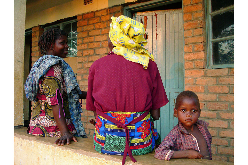 A child stares at the camera as two older people have tehir back to it