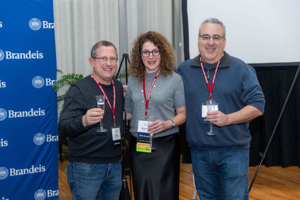 Three alumni from the class of 1990 hold champagne glasses in toast